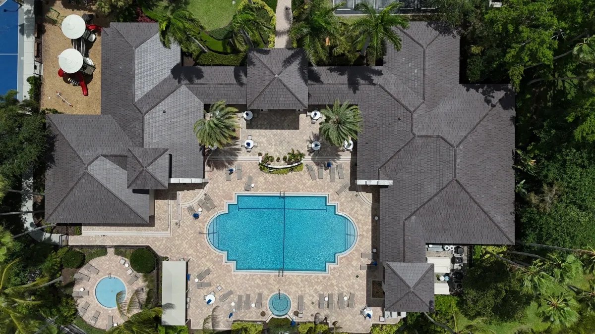 Overhead drone view of a finished dark tile roof on an HOA clubhouse surrounding a pool deck in Palm Beach County, Florida