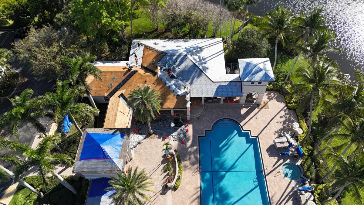 Drone view of a clubhouse roof mid tear-off with exposed wood decking, new underlayment on part of the roof and a roofing crew at work