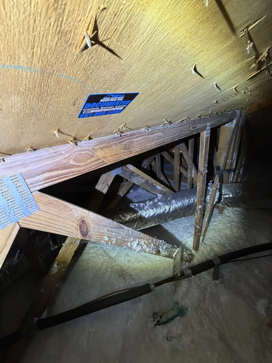 Wide attic view showing tagged roof decking, wood trusses, metal plates, ductwork and insulation.