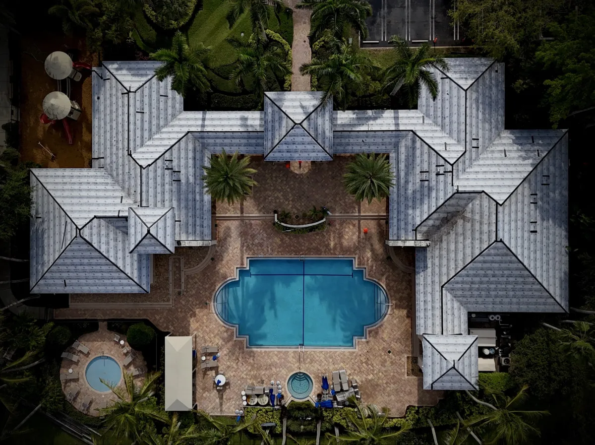 Straight-down drone view of a clubhouse roof fully covered in new underlayment around a pool and patio before tile installation