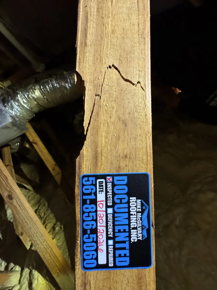 Close-up of a cracked attic framing member next to an MMR Documented inspection tag.
