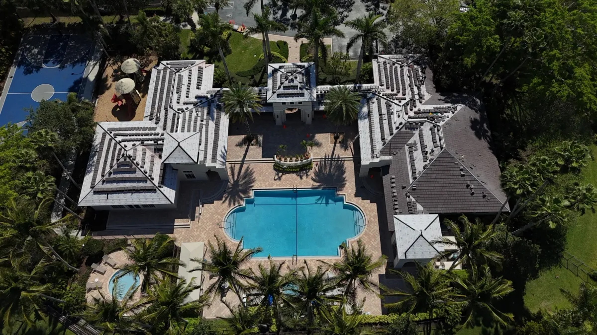 Angled drone view of a clubhouse roof during tile installation with finished dark tile on one wing and stacked tile on the others