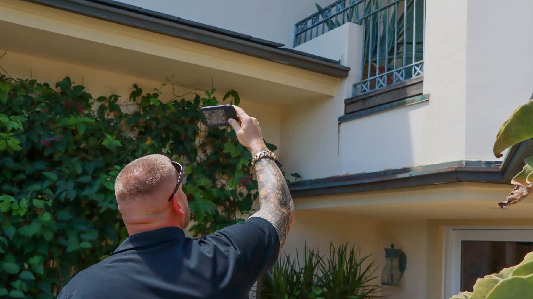 Roofing contractor photographing roof-edge and wall conditions during a field inspection