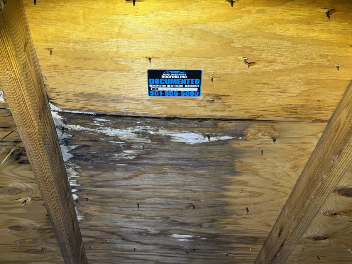 Wide view of water-stained plywood roof decking between attic framing, with an MMR Documented tag above the stain.