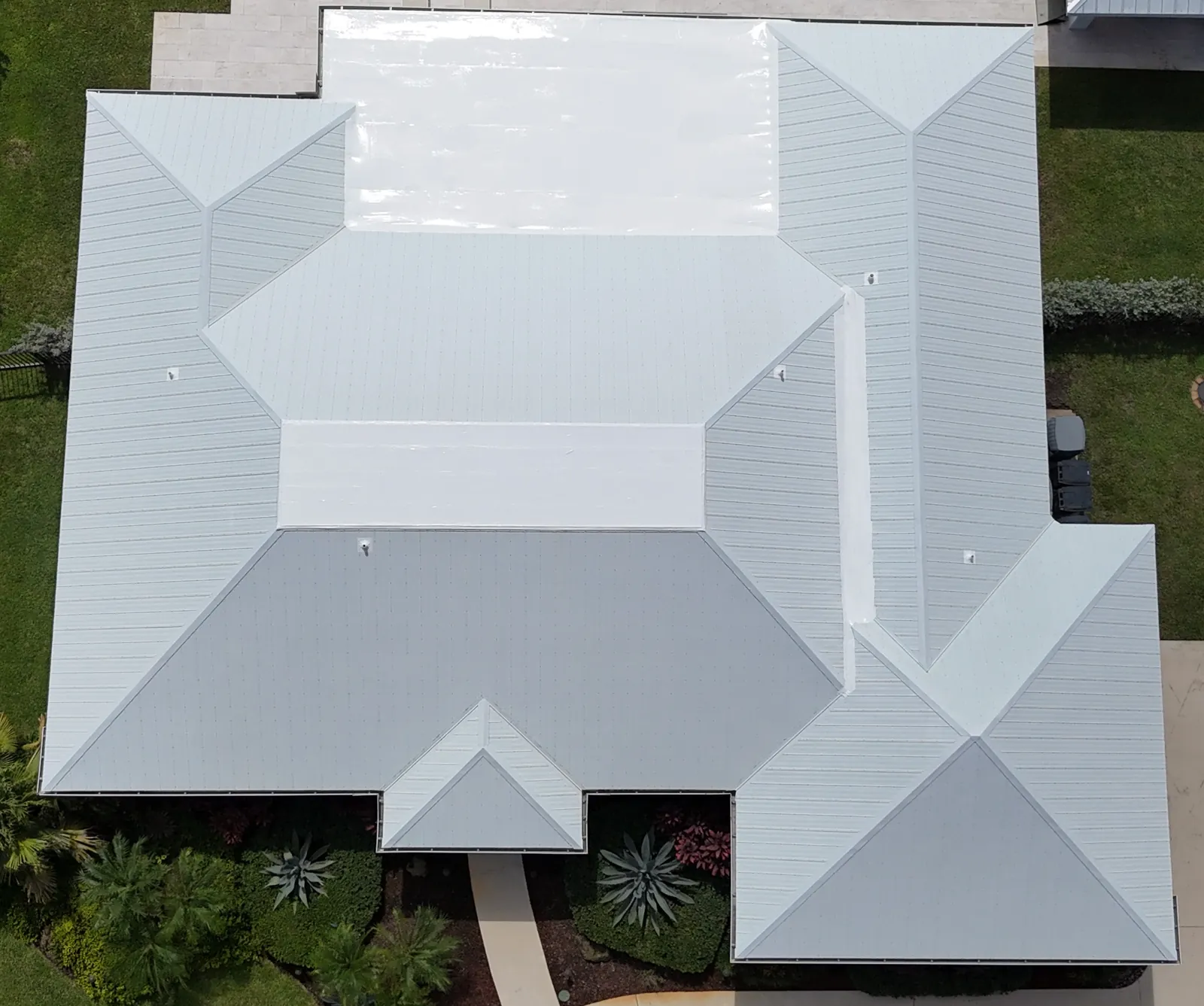 Drone photo from directly above Emily S.'s Jupiter home after the repair: a light gray metal roof with the glossy white restored flat section at the back.