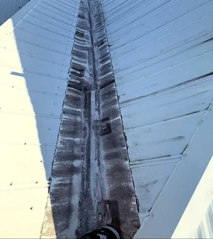 Before work: the metal-to-flat transition, a stained strip between two metal roof slopes.