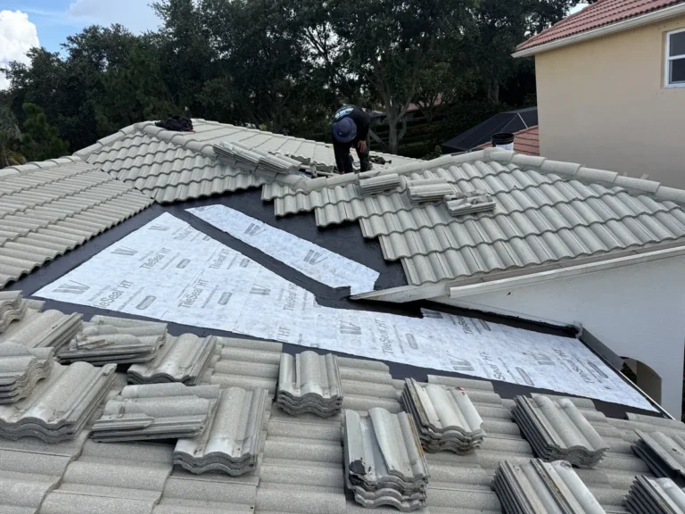A roofer working above the long valley, now lined with new white self-adhered underlayment, with the tiles stacked to go back on.