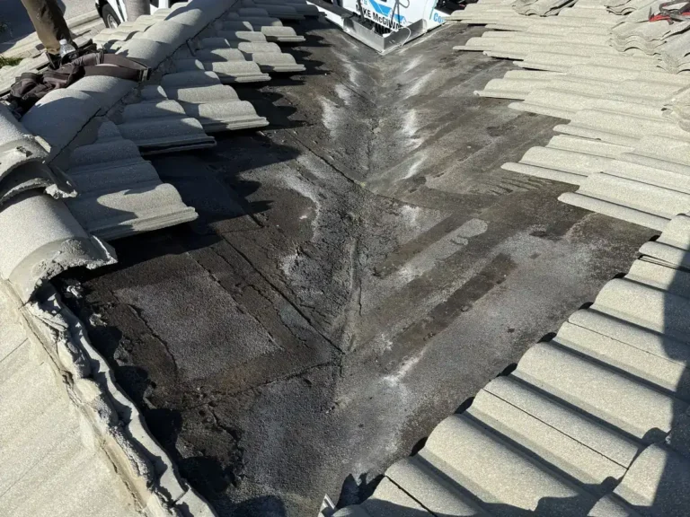 A street-side roof valley opened up, with the old underlayment stained where the water runs. Mike McGilvary Roofing trucks are parked below.