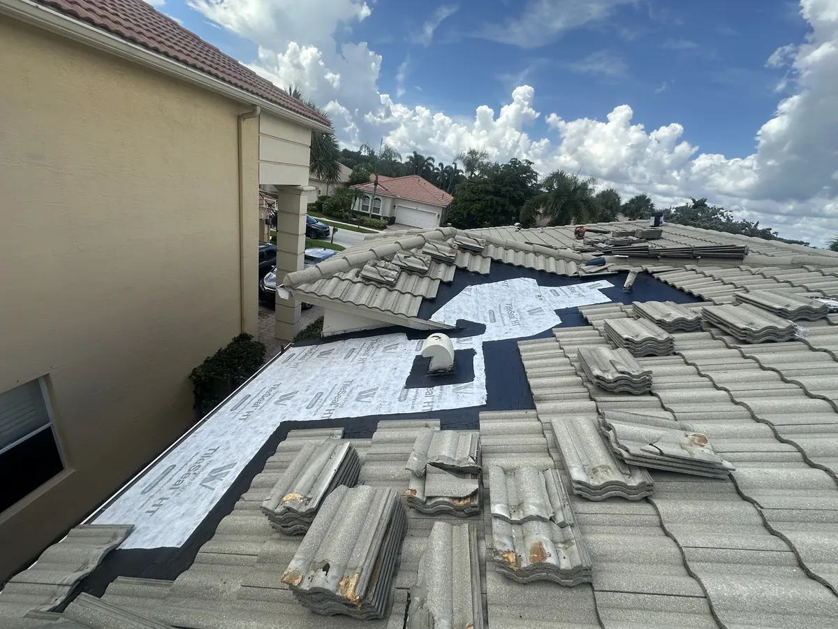 A rebuilt roof section covered in new white self-adhered underlayment, with the existing tiles stacked nearby to go back on.