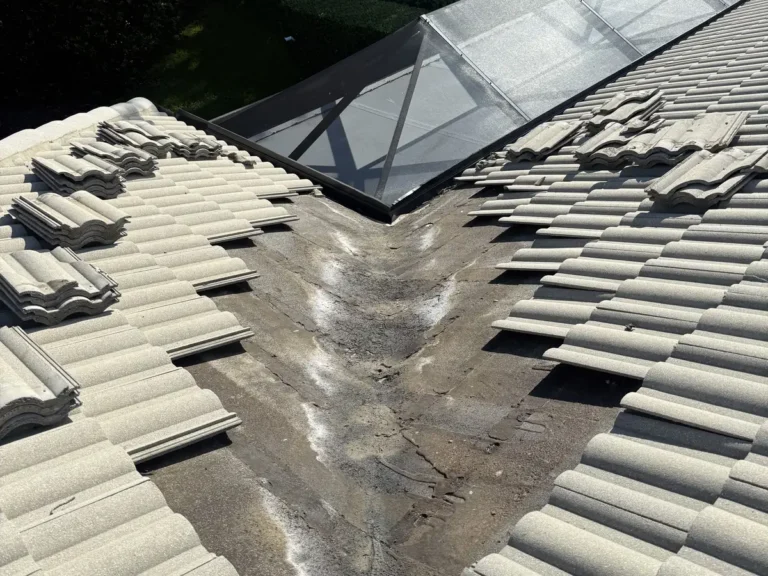 The valley beside the glass pool enclosure opened up, with the old underlayment stained and worn where the water runs.