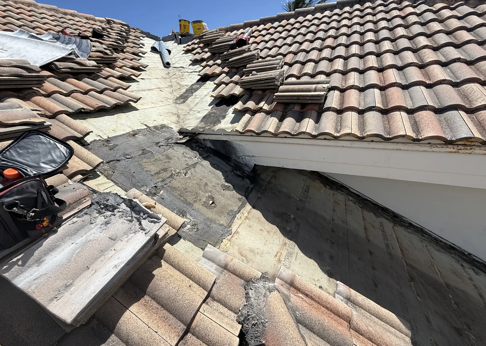 Palm Beach Shores tile roof opened at a failed tar patch, showing the compromised underlayment beneath the tile