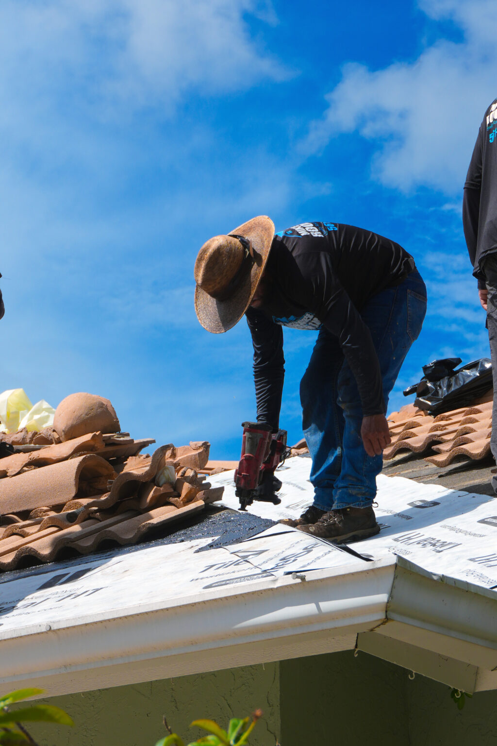 A roofer fastening new underlayment with a nail gun on an opened tile roof section