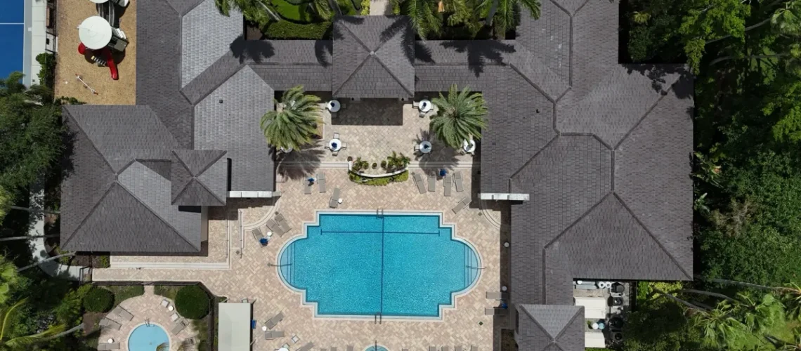 Overhead drone view of a finished dark tile roof on an HOA clubhouse surrounding a pool deck in Palm Beach County, Florida