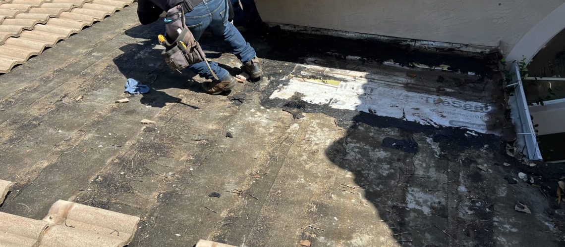 A crew member working on a low-slope roof section beside a tile roof